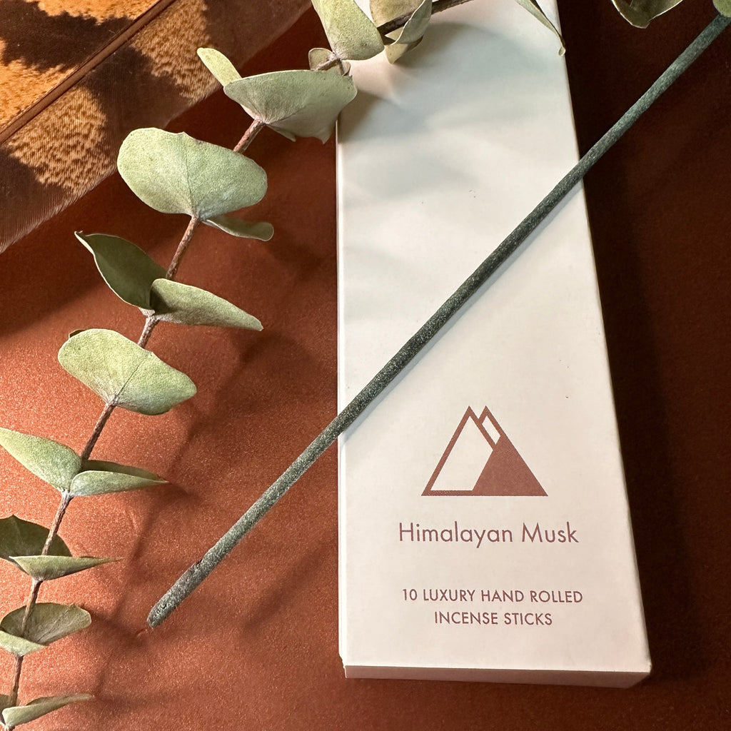 Sacred Elephant Himalayan Musk Räucherstäbchen – Packung mit Eukalyptuszweig auf bronzefarbener Fläche im warmen Tageslicht.