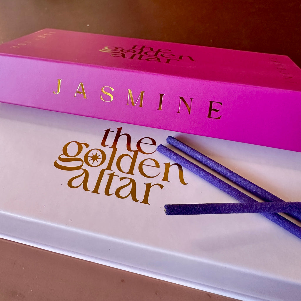 The Golden Altar Jasmine Räucherstäbchen – pink-goldene Box auf weißem Untergrund mit violetten Stäbchen, luxuriös und feminin.