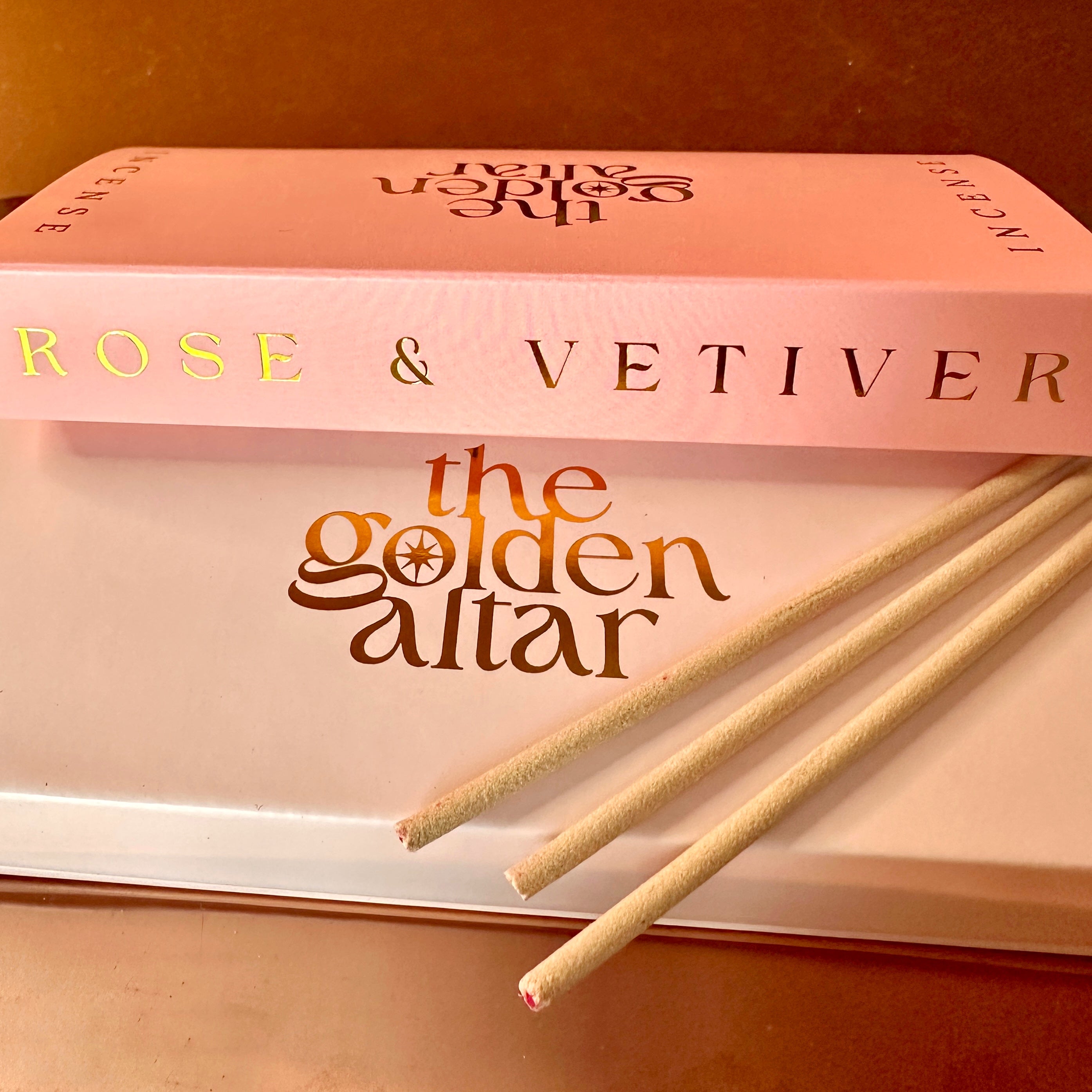 The Golden Altar Rose & Vetiver Räucherstäbchen – sonniger Duft mit hellrosa Verpackung und goldener Folienprägung auf weißem Untergrund, luxuriös und warm.