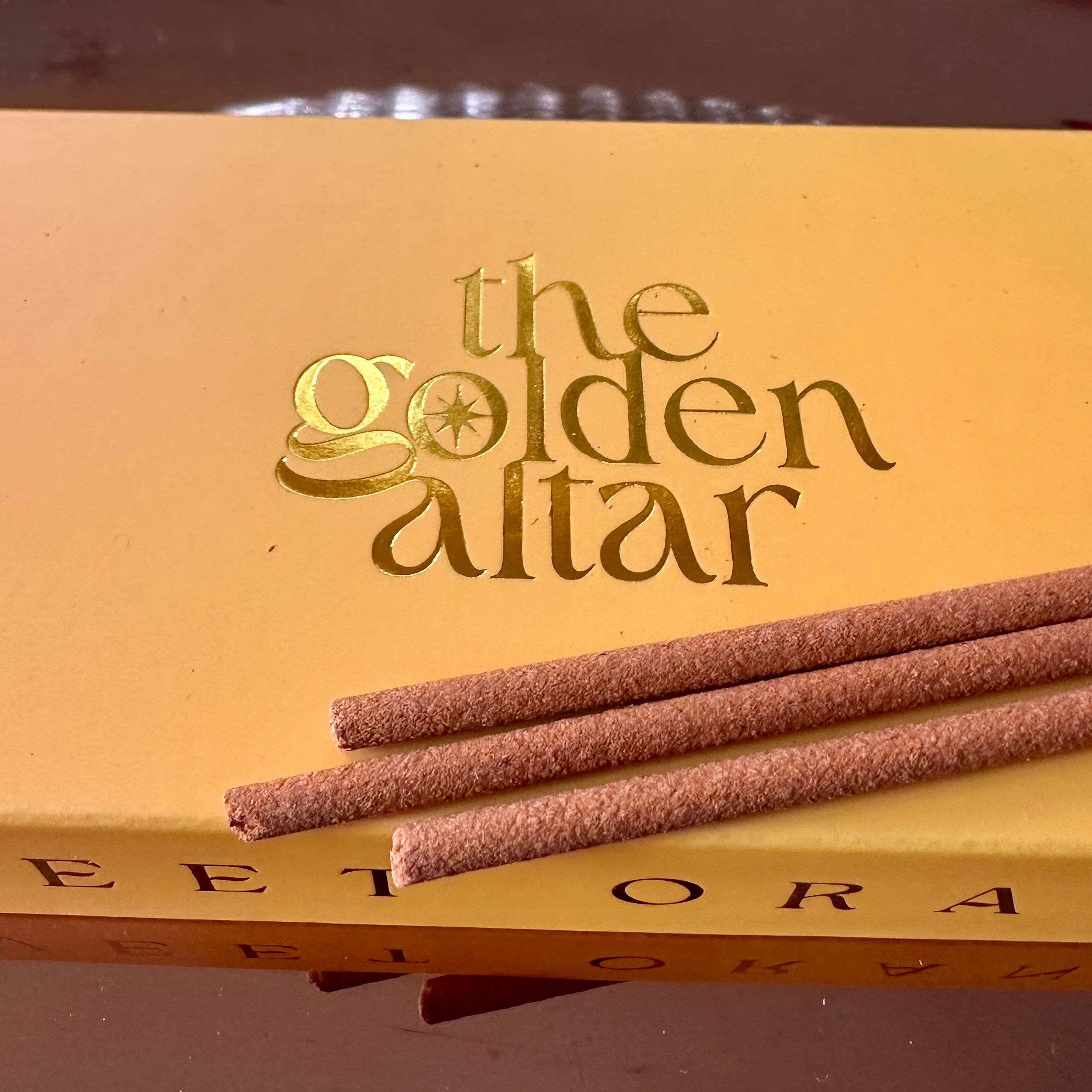 Detailaufnahme der The Golden Altar Sweet Orange Verpackung mit Goldprägung und Räucherstäbchen – warmes, strahlendes Licht.