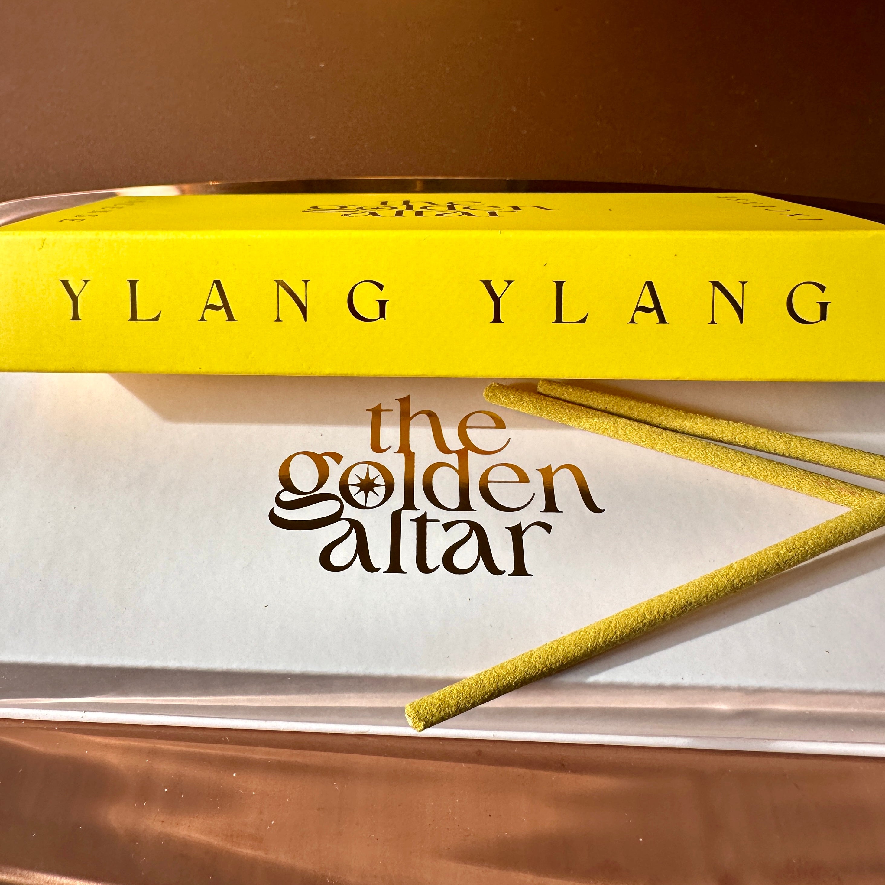 The Golden Altar Ylang Ylang Räucherstäbchen – goldgelbe Schachtel mit braunem Logo und zwei Stäbchen auf weißem Untergrund, sinnlich und warm.
