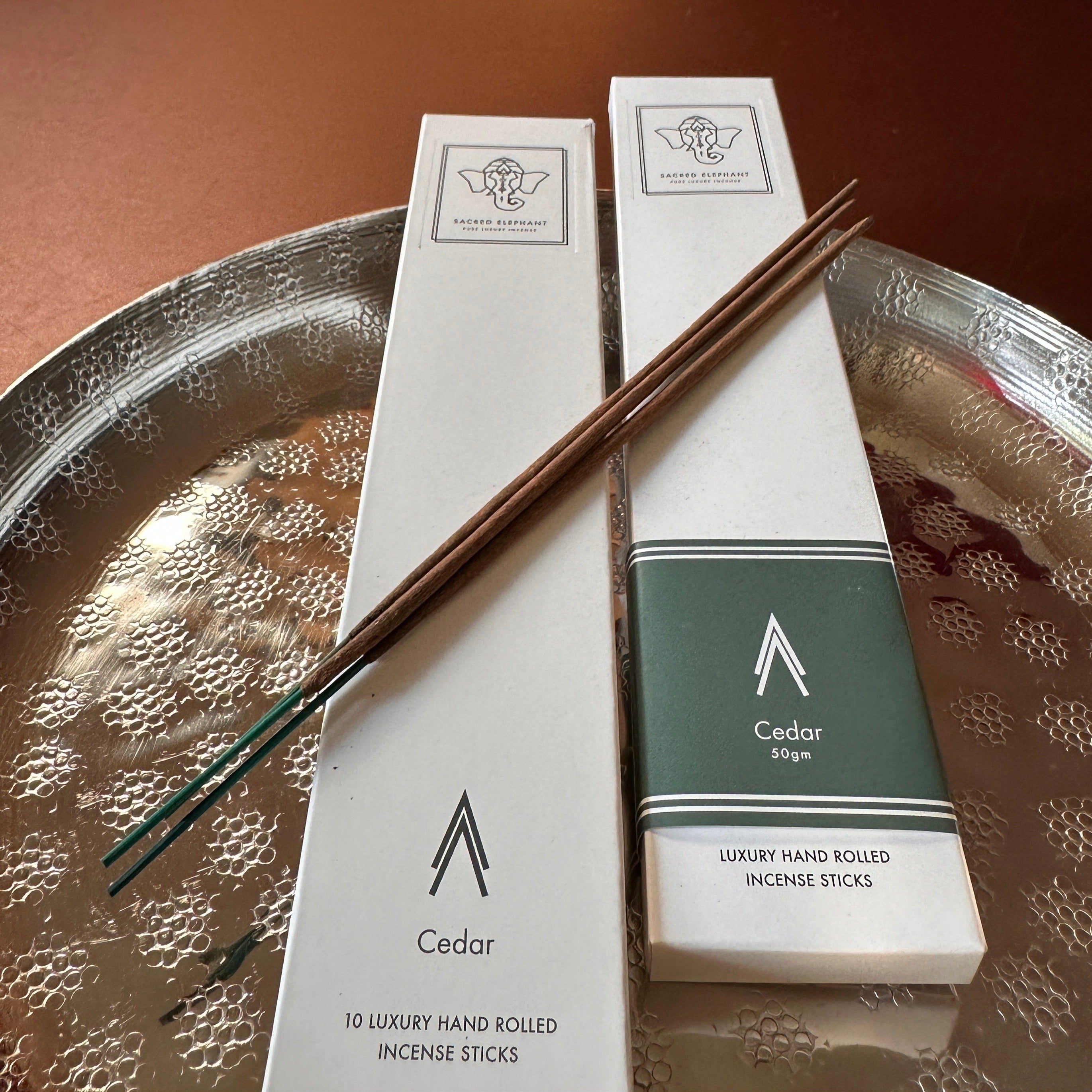 Sacred Elephant Cedar Räucherstäbchen im Doppelpack auf Tablett – minimalistisches Design mit grünem Etikett und Holzstäbchen.