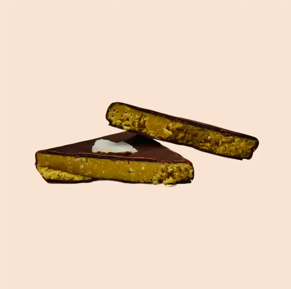 Aufgebrochene Kokos-Kurkuma-Praline – dunkle Schokolade mit cremigem Mandelkern, Kokos-Crunch & wärmender Gewürzmischung. Clean, vegan & soulful.